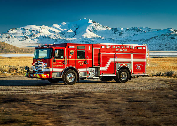 The driver's side of an Enforcer pumper parked in front of a snow-covered mountain.