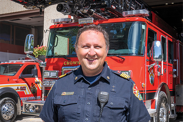 The Chief of Crowsnest Pass Fire Rescue standing in front of an Enforcer 110' Ascendant Aerial Platform at the fire station.