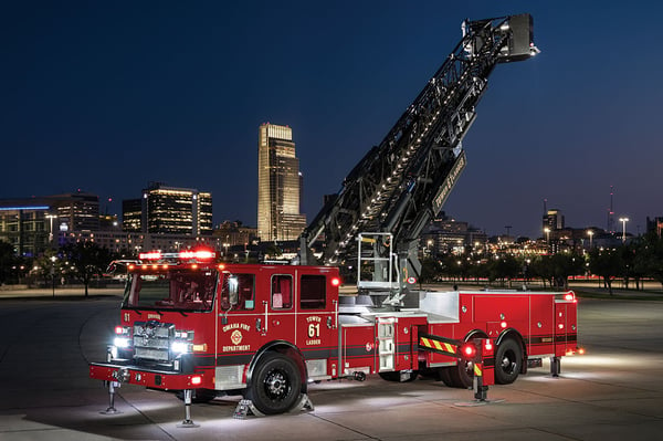 An Enforcer Ascendant 100 Aerial Tower with the lights on in front of a city skyline at night with the aerial extended up.