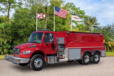 A red Pierce BX tanker is parked on an angle with green foliage and three flags in the background. 