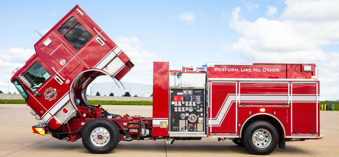 A red Pierce Volterra electric fire truck is parked with the cab tilted up showing the operational components on board the truck. 