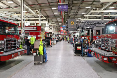 A manufacturing floor with a number of fire trucks being worked on and a visible number nine on a gray background.