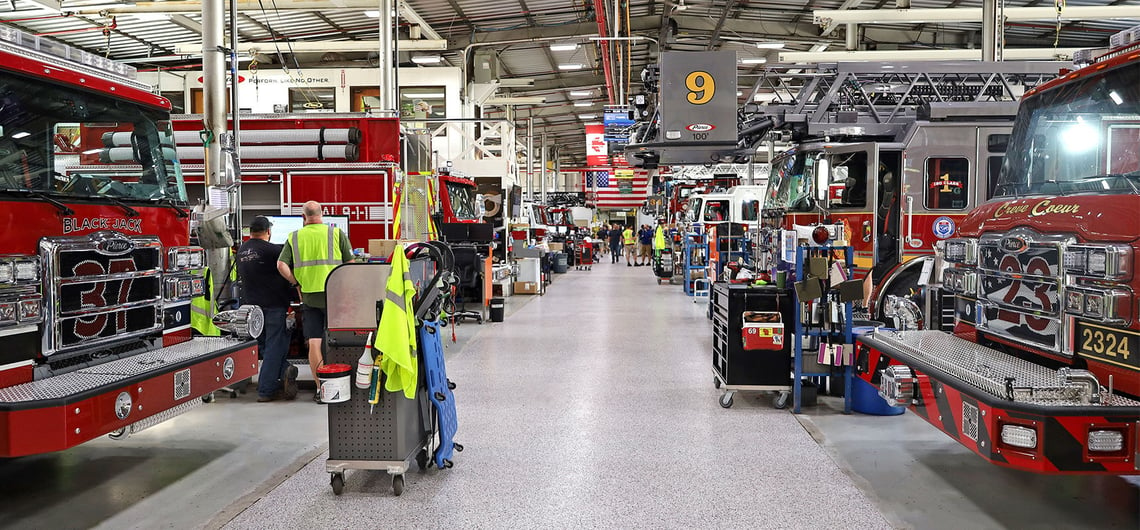 A gray fire truck manufacturing floor lined with red fire trucks on each side.