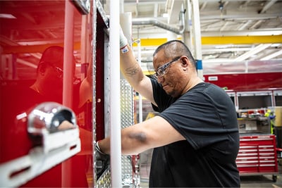 An employee in a black shirt works on the final assemble of a red fire truck.