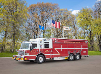 A red South Hill Volunteer Fire Department truck in a parking lot with flags and trees behind it