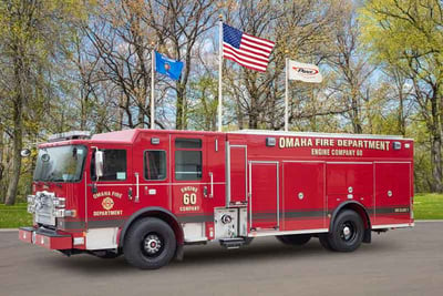 The red Omaha Fire Department pumper truck is parked with green trees in the background.