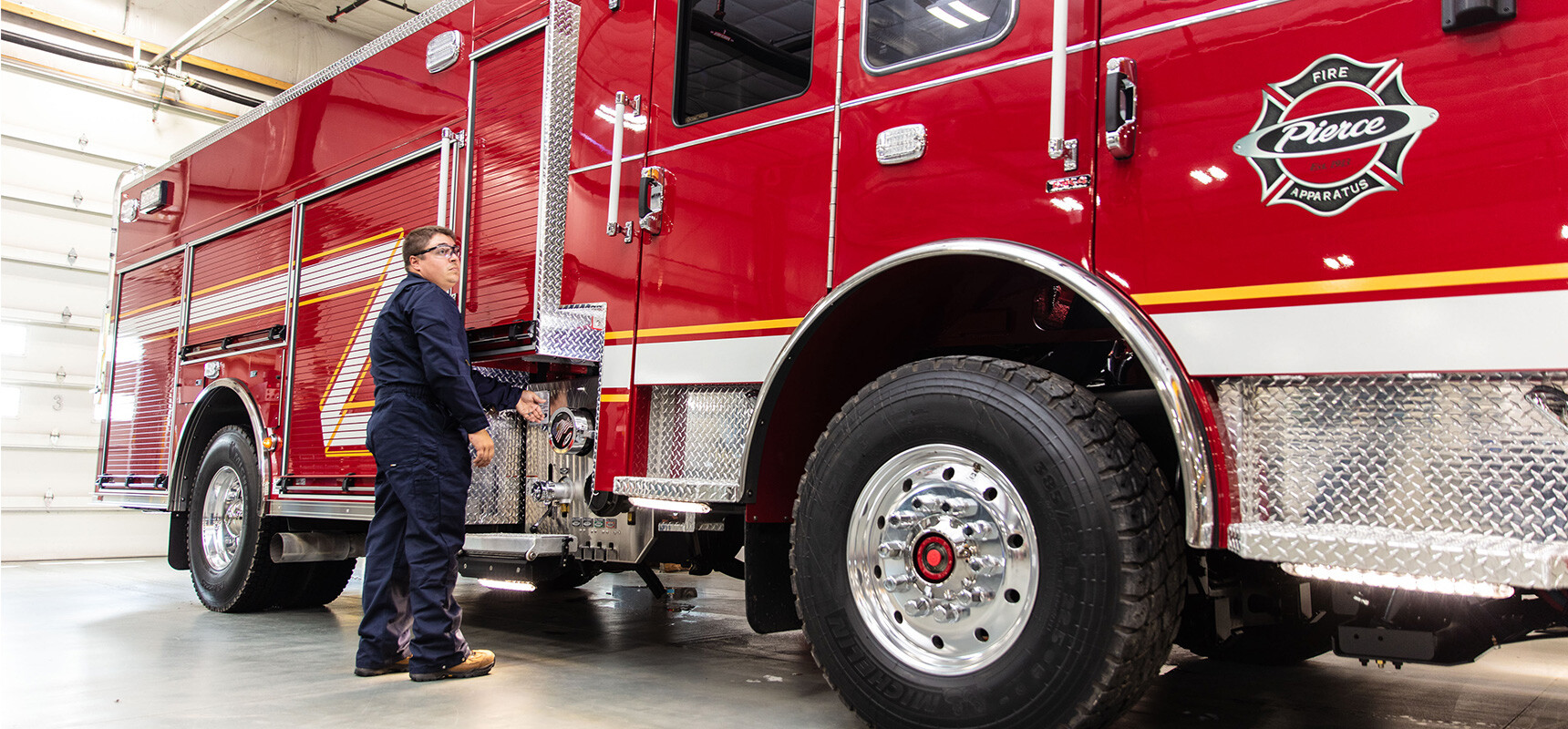 A red Pierce fire apparatus with service technician in a blue jumpsuit working on the apparatus.