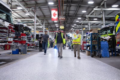 Three employees walking on the manufacturing floor with fire trucks on the site and a Canadian flag in the background.