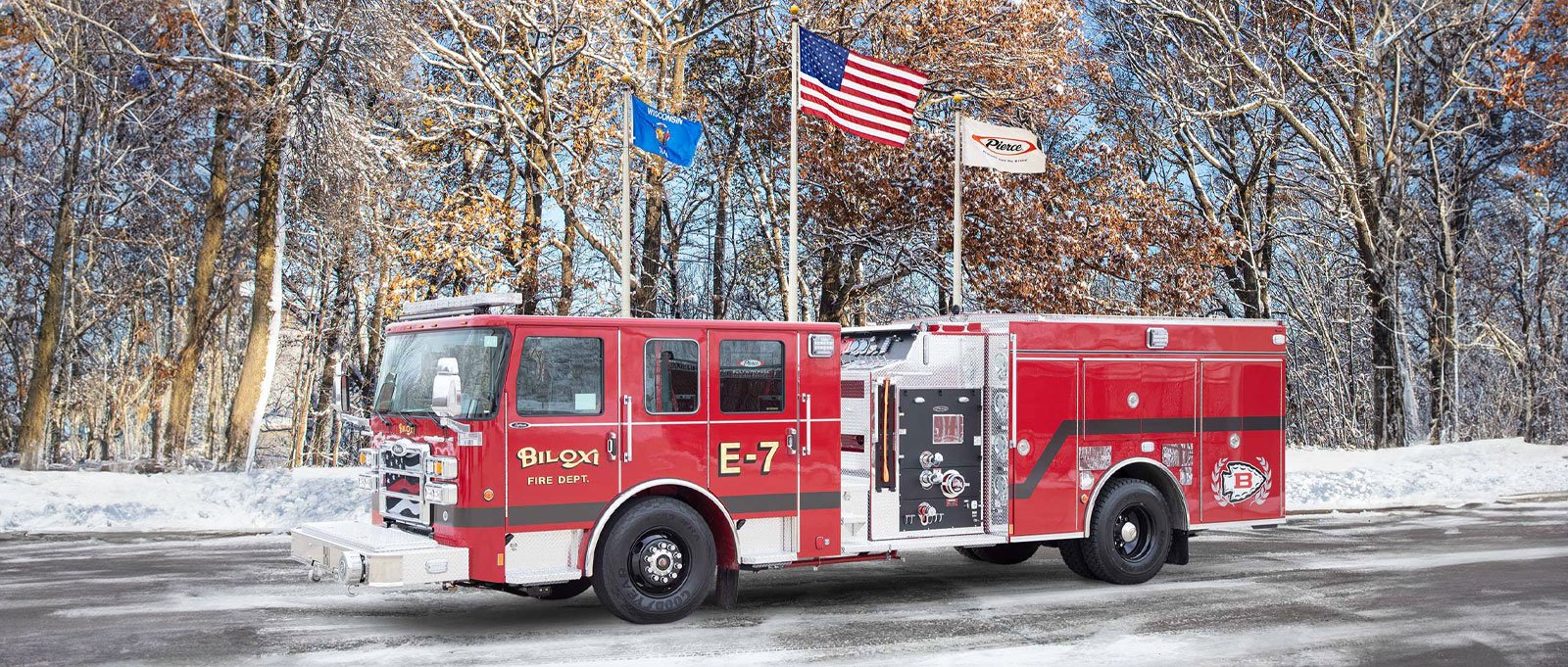 The red Biloxi Fire Department E-7 pumper is parked outside on an angle with snowy woods in the background. 
