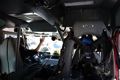  The interior cab of an electric fire truck shows the operator reaching for overhead controls.