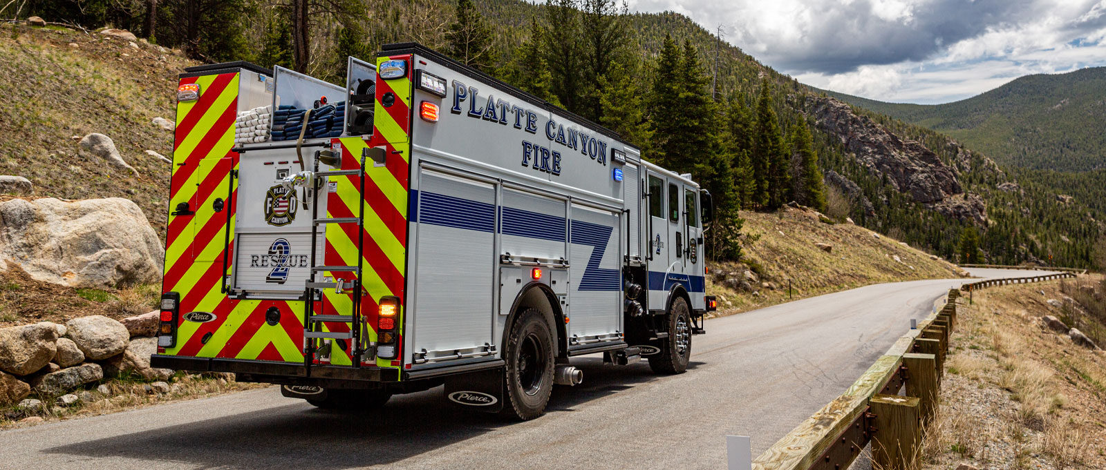 A red and neon yellow striped back end of a white and blue fire truck driving down a hill on the side of a mountain.