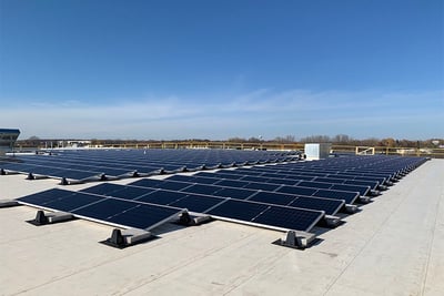 Dark solar panels are shown on the rooftop of a fire truck manufacturing facility with blue sky in the background. 