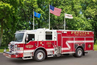 The red and white Prosper Fire Department pumper apparatus is parked on an angle with leafy green trees in the background.