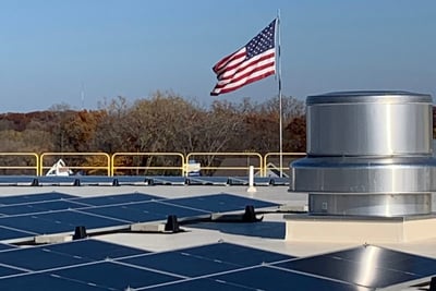 A close up image of several solar panels on top of a Pierce Manufacturing building with an American flag blowing the wind.