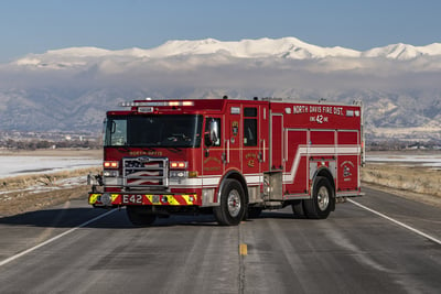 A red fire truck on a flat pavement road with snow capped mountains in the background, with a blue sky.