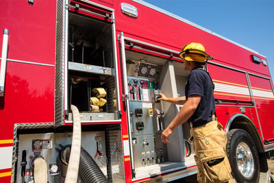 A fire fighter working on gauges on the side of a red fire truck.