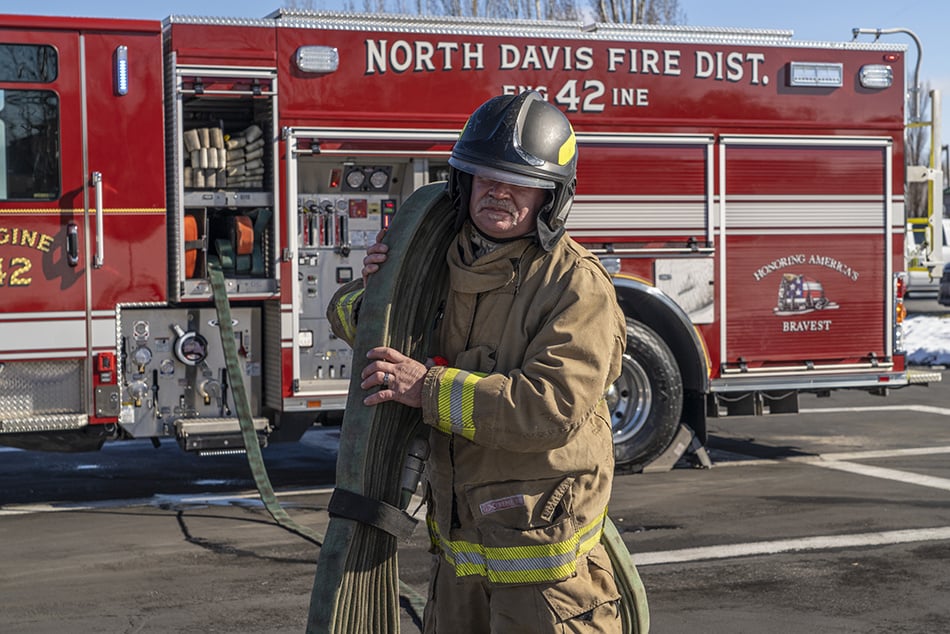 A firefighter in turnout gear pulling hose off of a fire truck from the crosslays.