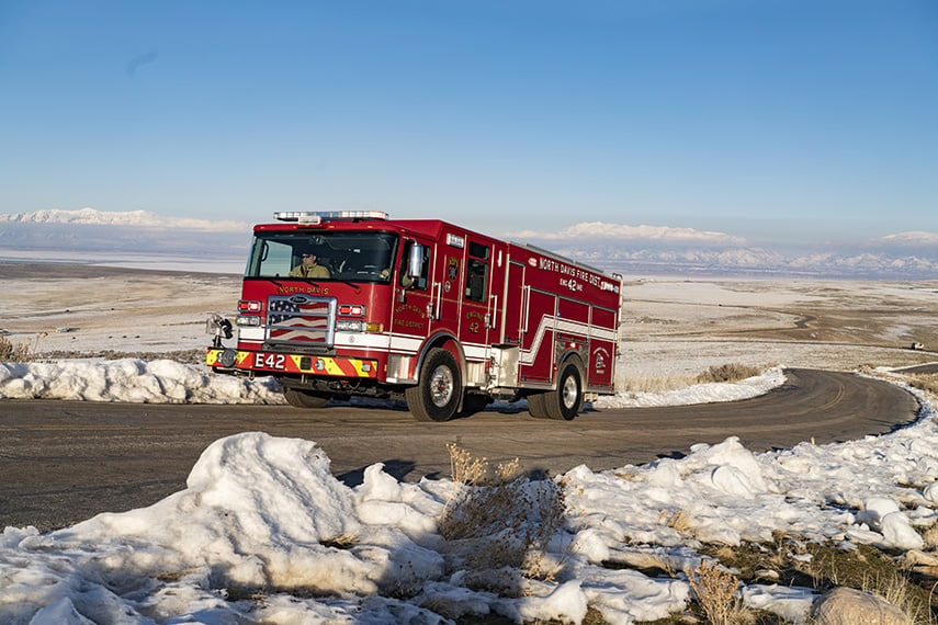 An Enforcer pumper driving on a paved road with snow on the ground and mountains in the background.