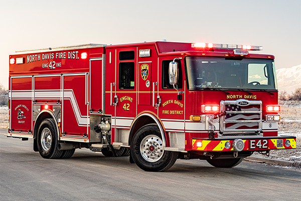 The officer's side of an Enforcer pumper with its lights on parked in front of a frosty field.