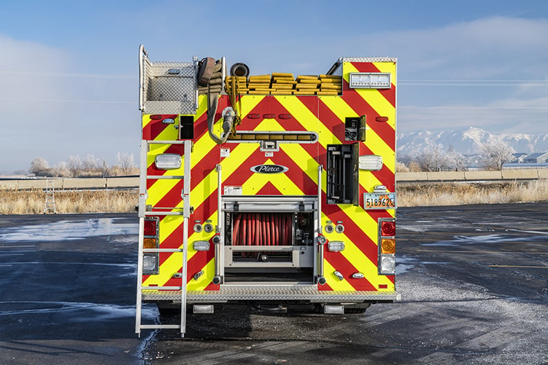 The rear of a pumper with a ladder extended, hose in the hosebed and a compartment open showing a booster reel inside.