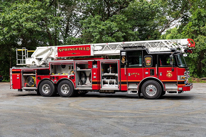 The Officer's side of an Arrow XT 100' Heavy-Duty Low-Profile Steel Aerial Ladder with the compartment doors open showing equipment.