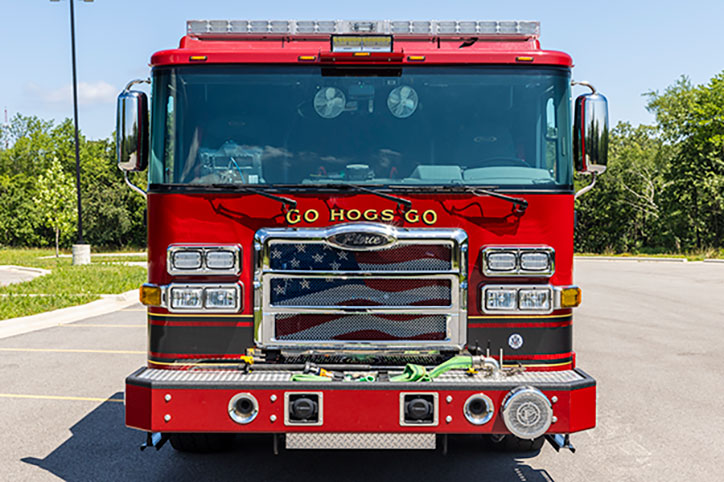 A Pierce fire truck with an American flag on the grille and a graphic above the grille that says, 