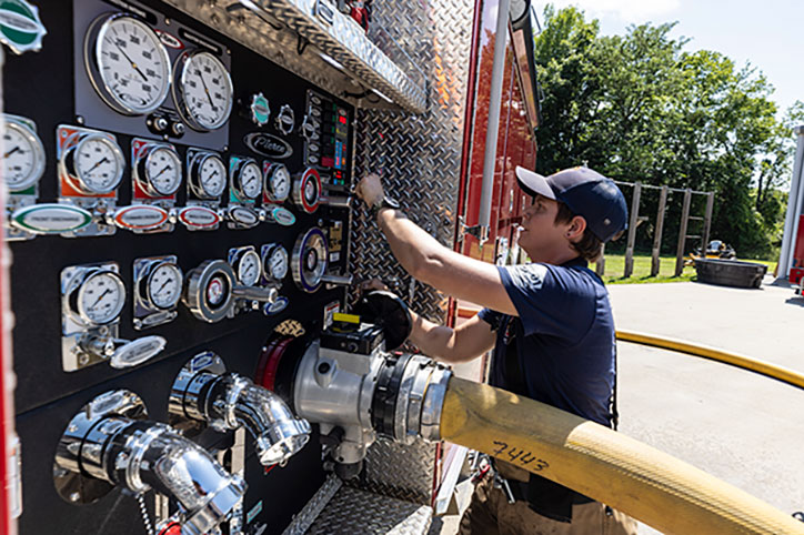 A firefighter operating the pump panel of a Pierce fire truck with a hose connected to it.