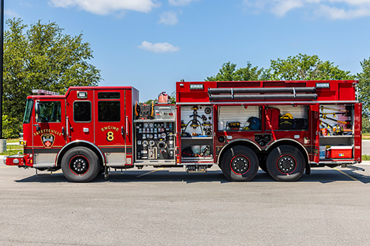 The driver's side of a Pierce Enforcer Custom Dry-Side Tanker parked in a parking lot with compartments open showing equipment.