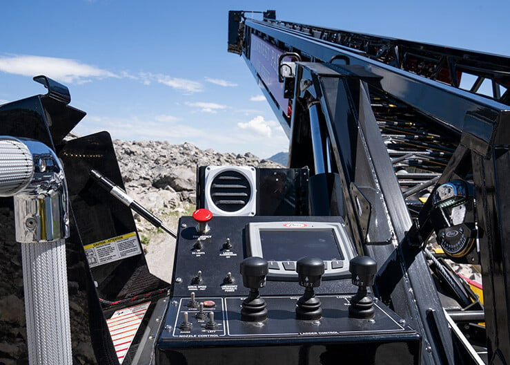 The aerial operator controls at the base of an Ascendant 110’ Aerial Platform with the ladder extended over a mountain.