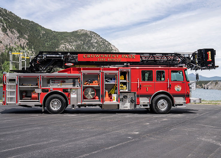 The officer's side of an Enforcer 110’ Ascendant Heavy-Duty Aerial Platform with the compartments open showing tools and equipment parked in front of a lake.