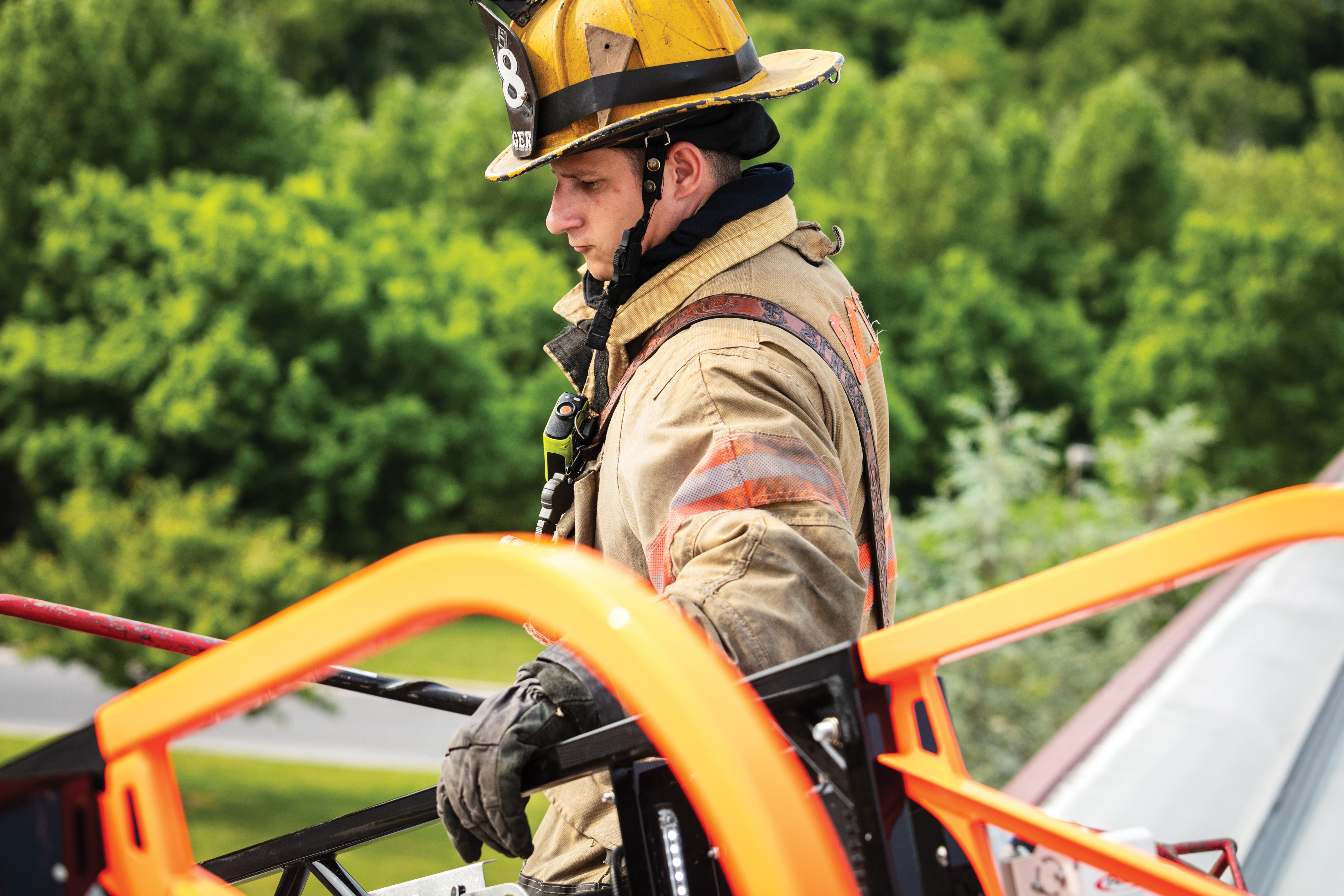 A firefighter on a rooftop with his hand on the ladder of a firetruck.