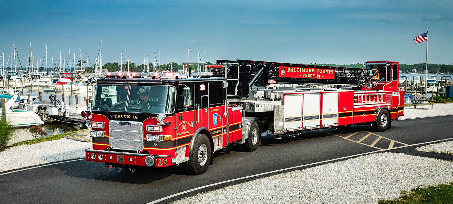 The front driver's side of Baltimore County Fire Departments Ascendant 107' Heavy-Duty Tiller Aerial Ladder by a marina.