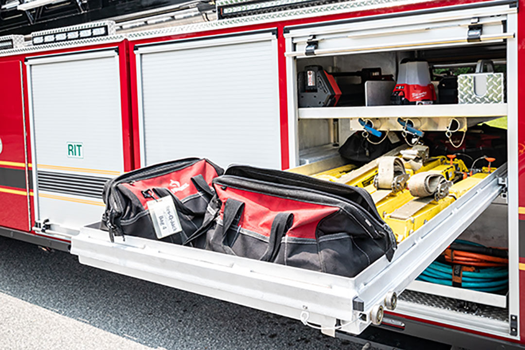 Heavy-Duty Tiller Aerial Ladder compartment with a slide out tray extended out with firefighting equipment stored on it.