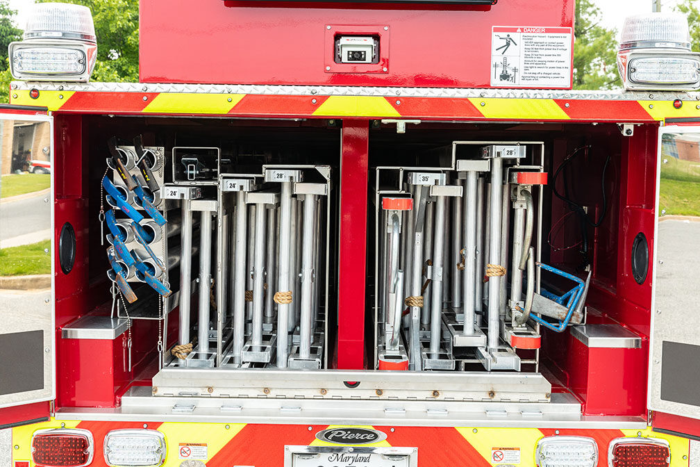 The rear of a Heavy-Duty Tiller Aerial Ladder with the compartment doors open showing ladders inside.