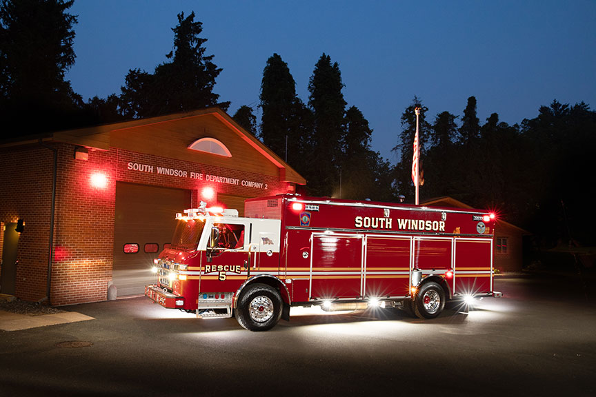 A Velocity Walk-In Heavy-Duty Rescue fire truck parked outside a fire station at night with its lights on.