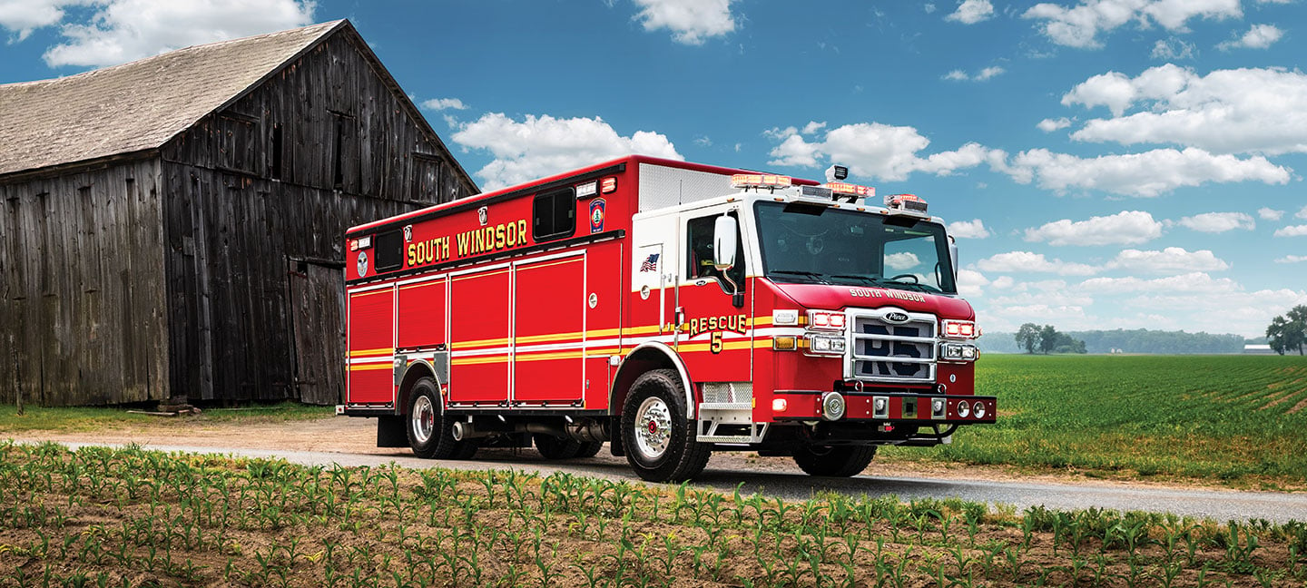 A Velocity Walk-In Heavy-Duty Rescue fire truck parked next to a barn and farm fields.