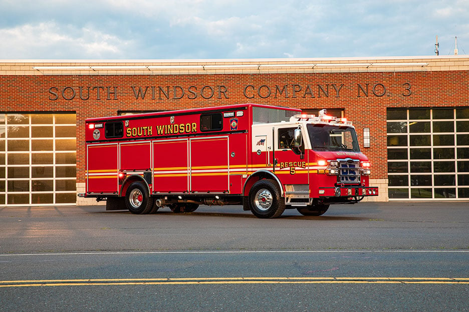 The Officer's side of a Velocity Walk-In Heavy-Duty Rescue fire truck parked at an angle in front of Fire Station Number Three.