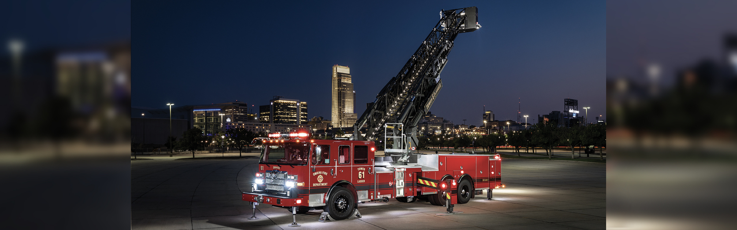 An Enforcer Ascendant 100 Aerial Tower with lights on in front of a city skyline at night with the aerial extended up.