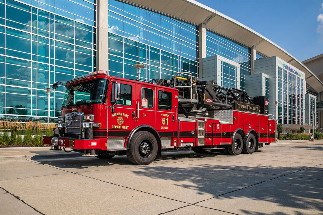 The drivers side of an Enforcer Ascendant 100 Aerial Tower next to a building with glass windows on a sunny day.