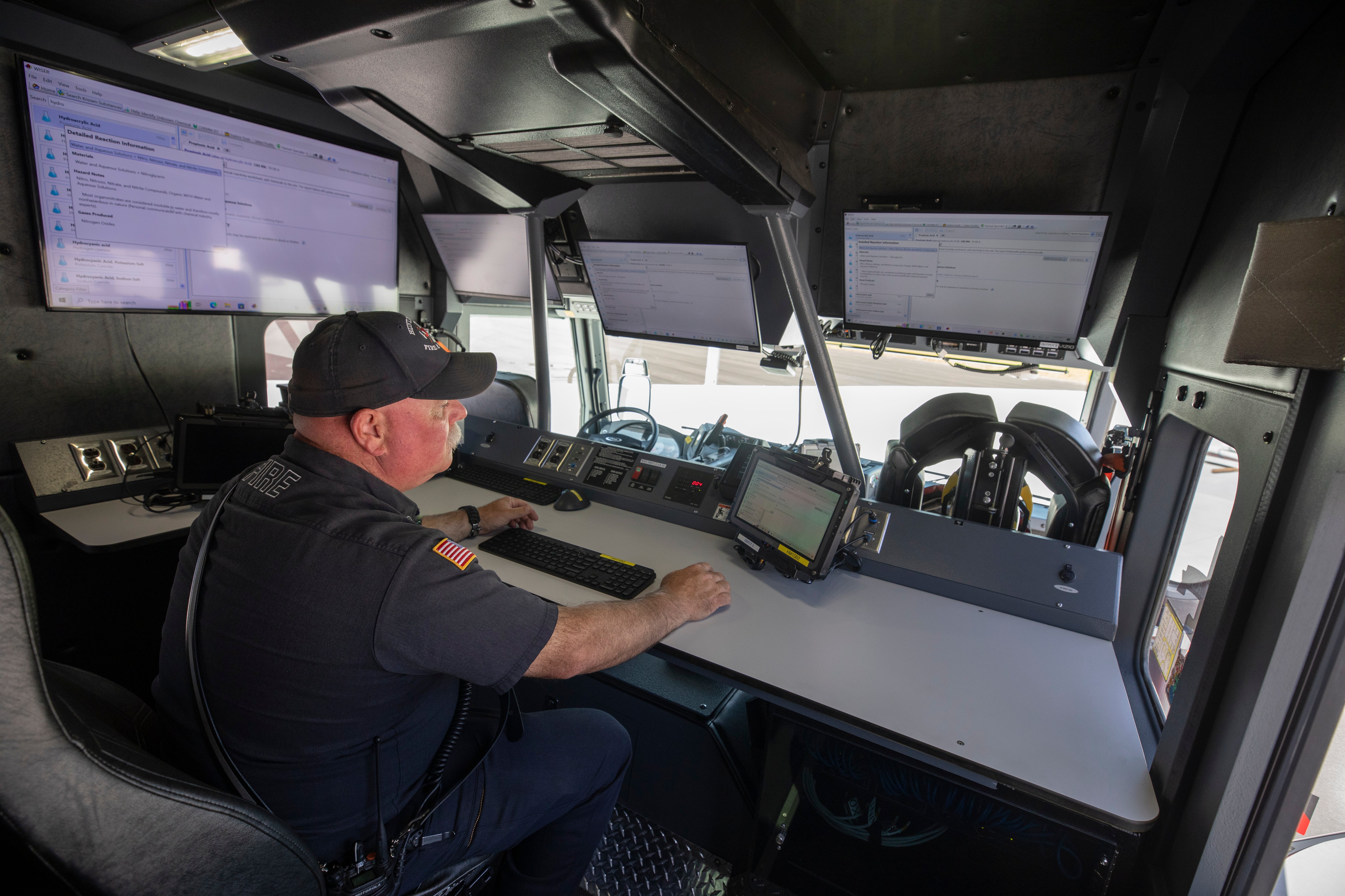 A firefighter working at a desk on a computer inside a heavy-duty rescue fire truck.