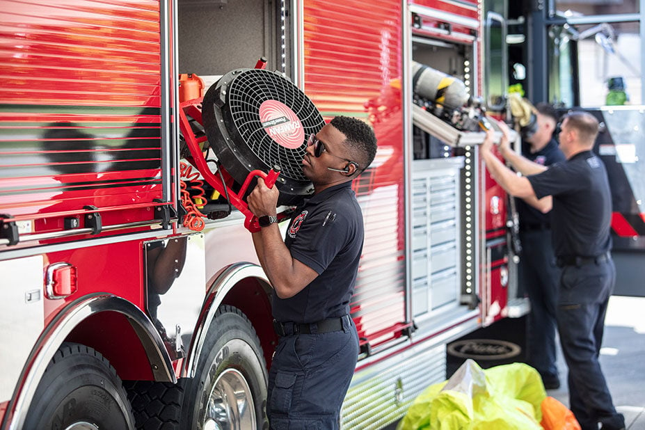 Firefighters retrieving equipment out of the compartments from the officers side of a fire truck.