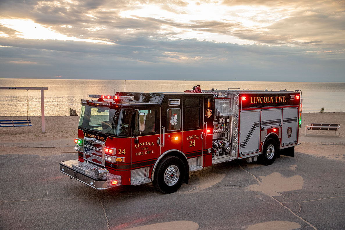 An Enforcer Heavy-Duty Rescue Pumper with the lights on in front of a beach on a cloudy day.