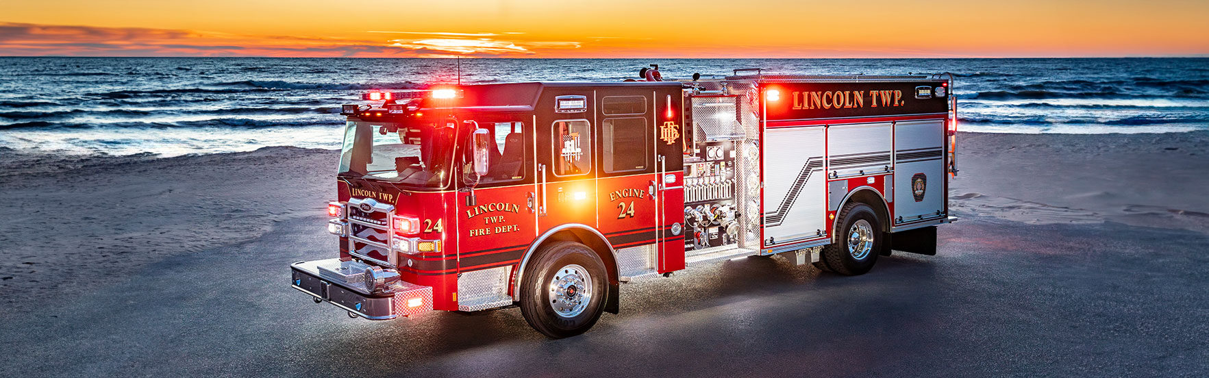 An Enforcer Heavy-Duty Rescue Pumper on a beach with the lights on in front of a sunrise with waves in the water.