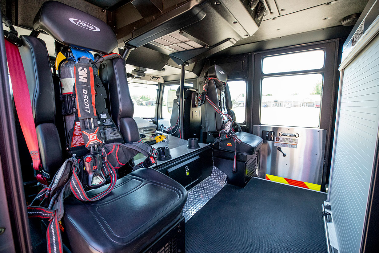 The crew cab of a fire truck with two rear facing seats and a compartment with a roll-up door.