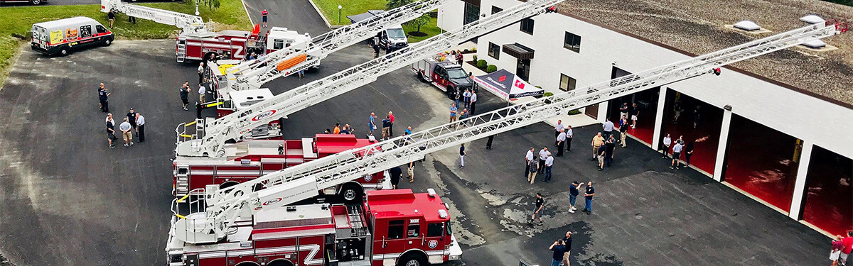 Fire Trucks in a line outside a fire station with the aerials extended.