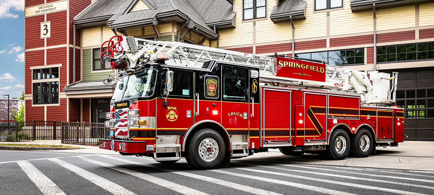 A 100' Heavy-Duty Low-Profile Steel Aerial Ladder driving out of a fire station.